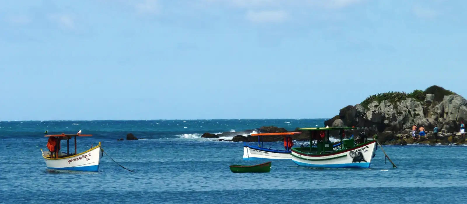 Barcos de pesca ancorados no mar da Armação, junto às pedras do costão