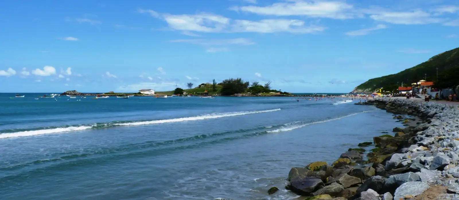 Mar calmo da Praia da Armação e a Ilha das Campanhas, ligada à orla por um caminho de pedras