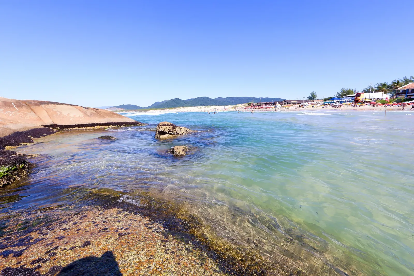 Piedras y agua clara en el rincón de la playa Joaquina, con la arena y los cerros al fondo
