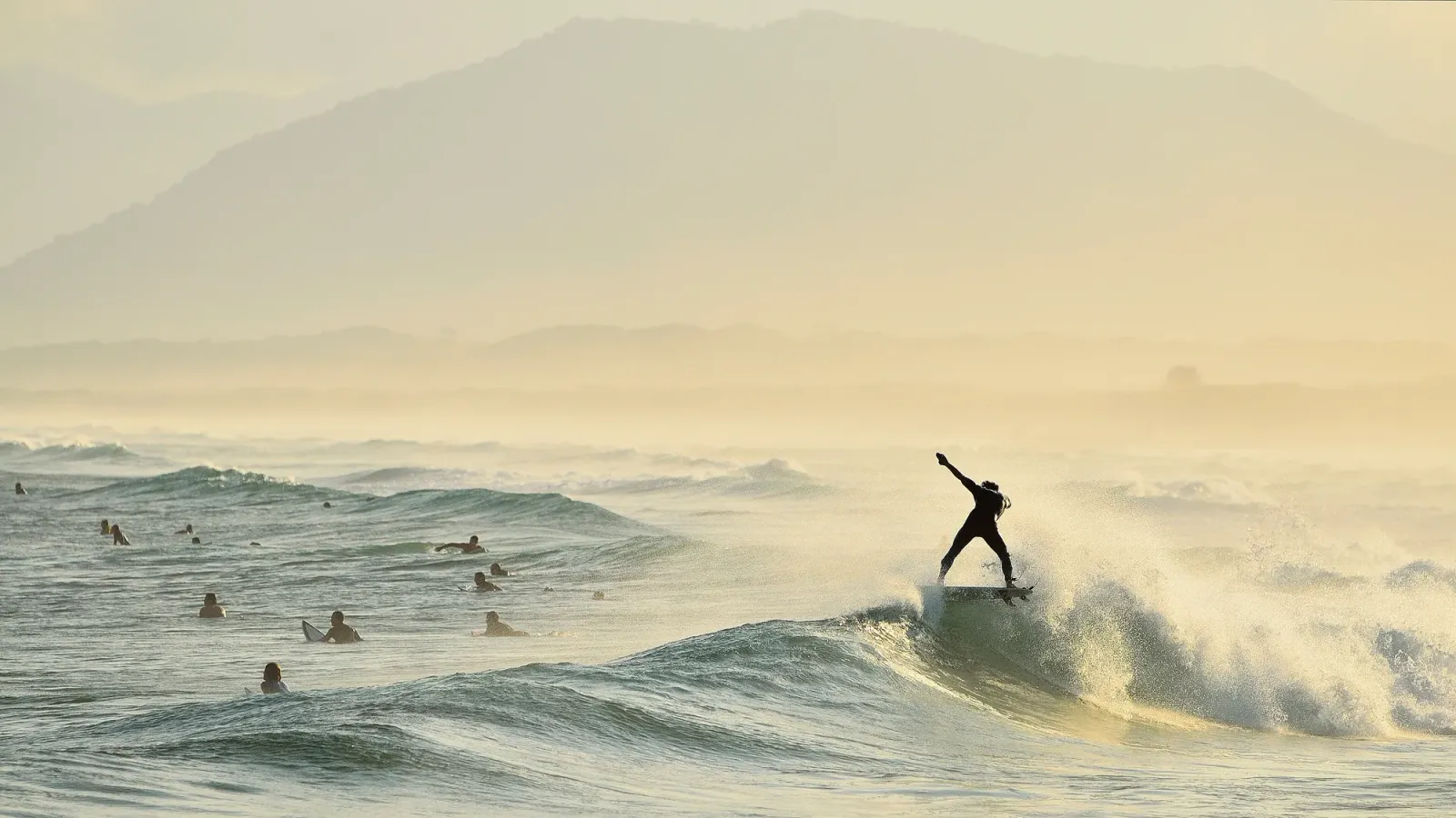 Surfista numa onda na Praia da Joaquina, com o morro ao fundo na névoa