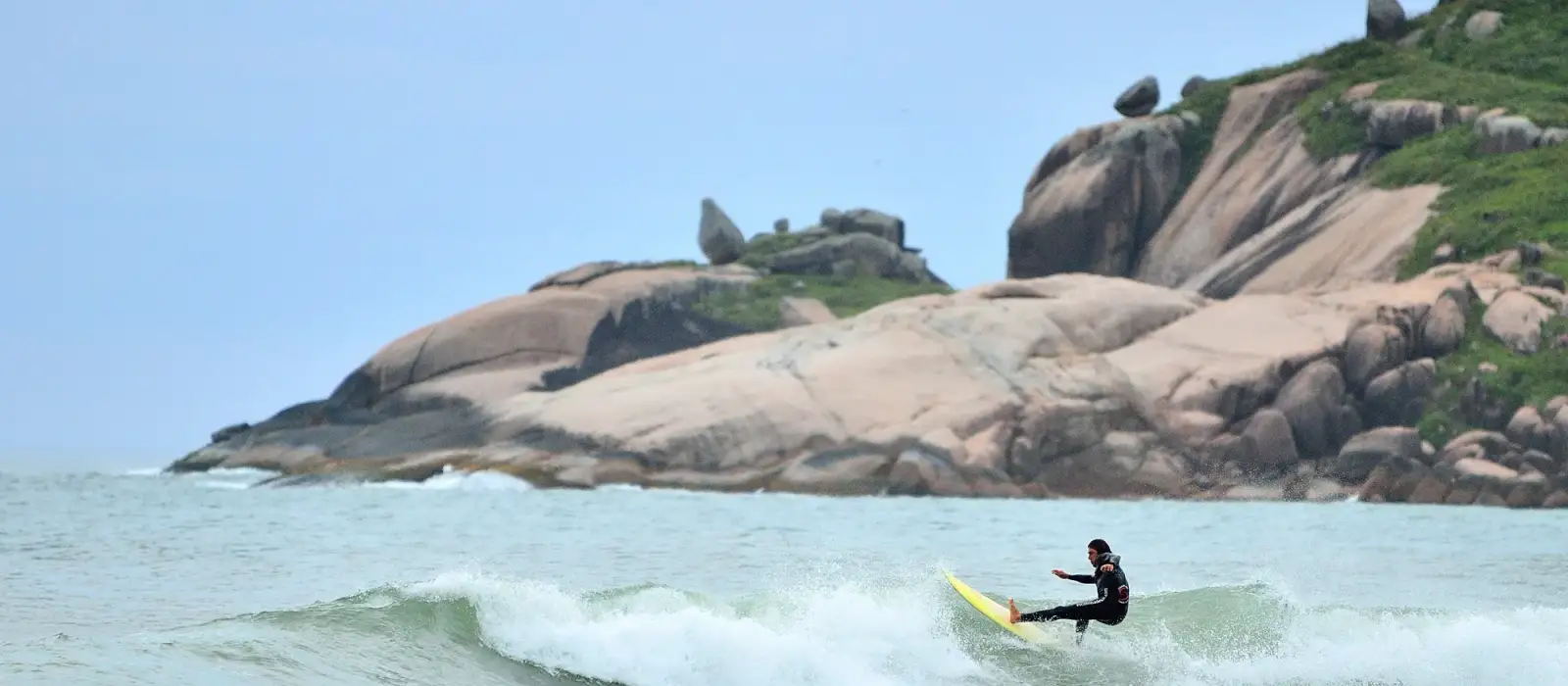 Surfista en una ola de la Praia Mole, con las piedras del rincón al fondo